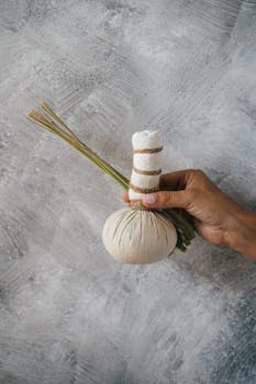 A close-up of a hand holding a herbal massage poultice with lemongrass, ideal for spa treatments.